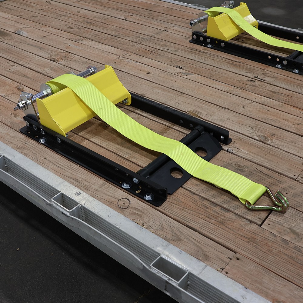 Yellow tie-down anchor with neon strap and metal hook on a wooden flatbed trailer deck.