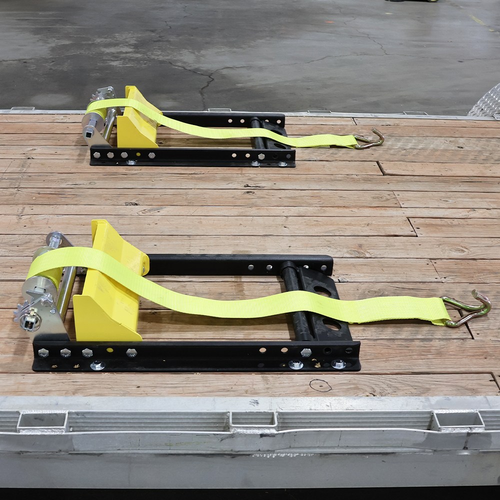 Yellow ratchet strap load restraints mounted on black metal frames on a wooden platform, ready to secure cargo in a trailer.