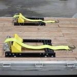 Yellow ratchet strap load restraints mounted on black metal frames on a wooden platform, ready to secure cargo in a trailer.